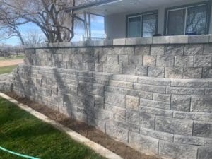 A multi tiered stone wall in the yard of a domestic residence in front of dark green grass done by Total Lawn Care & Landscape in Sterling, CO