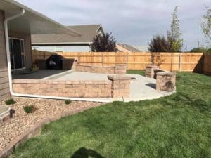 A stone and paved backyard patio leading to clean grassy lawn landscaped by by Total Lawn Care & Landscape in Sterling, CO