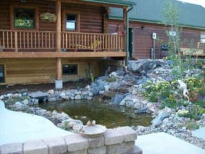 A pond surrounded by small stones and small flowers in front of a patio installed and designed by Total Lawn Care & Landscape in Sterling, CO
