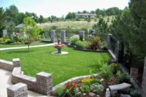 An ornate backyard featuring a small bird fountain in between three bursting flower beds surrounded by a stone and metal fence installed by Total Lawn Care & Landscape in Sterling, CO