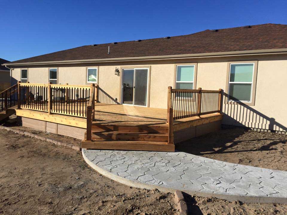 A wooden patio with two sets of steps leading to stone paths leading into newly churned backyards created by by Total Lawn Care & Landscape in Sterling, CO