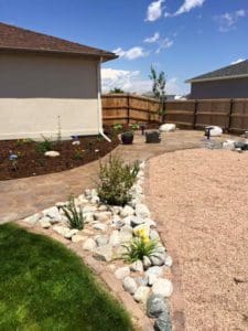 A stone path leading to a section of lawn with much and some flowers, a plain stone area, and a small rocky flower bed courtesy of Total Lawn Care & Landscape in Sterling, CO